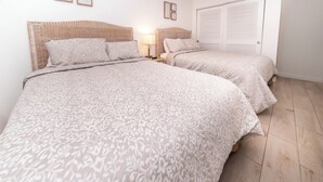 A bedroom with two beds, each with a patterned bedspread and pillows, a bedside table with a lamp, and a wardrobe with louvered doors.