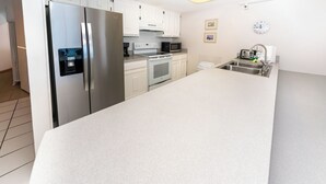 A modern kitchen with stainless steel appliances, white cabinetry, and a large countertop.