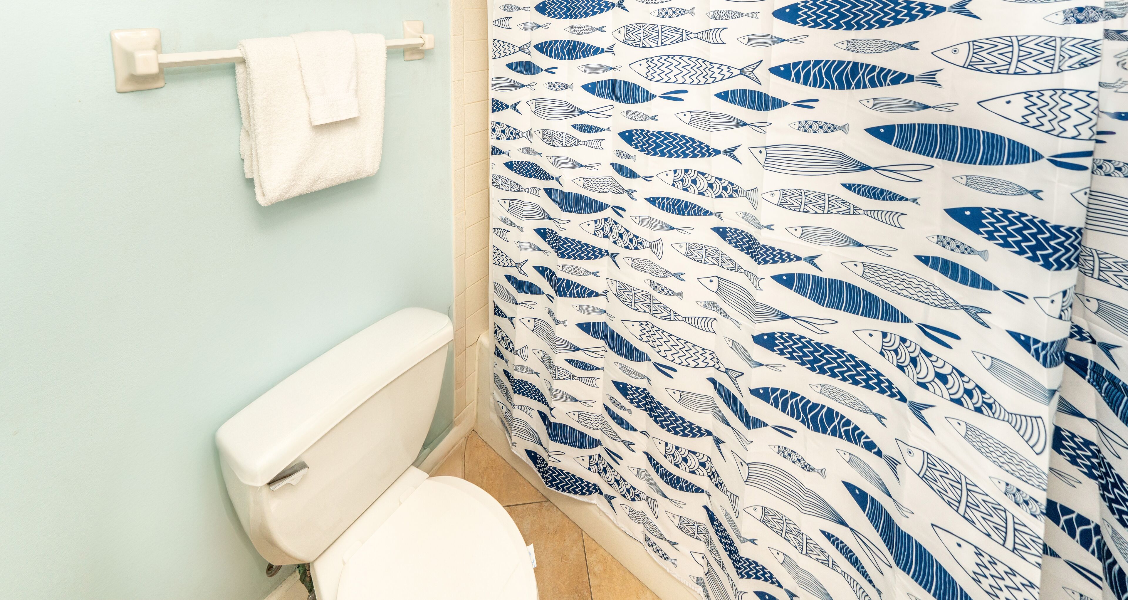 Un baño con inodoro, toallero y cortina de ducha con estampado de peces.