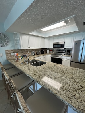 A modern kitchen with white cabinets, granite countertops, stainless steel appliances, and a built-in bar area with cushioned seating.
