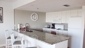 A kitchen with white cabinets, a granite countertop, a sink, and a clock on the wall.