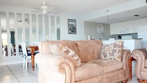 Ein Wohnzimmer mit einem beigefarbenen Sofa, einem Essbereich mit Holztisch und Stühlen, und einer Küche im Hintergrund.