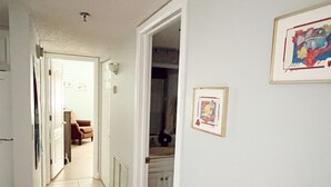 A hallway with white walls and a tiled floor leading to a kitchen area.