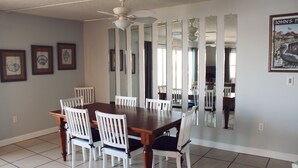 A dining room with a wooden table and white chairs, a ceiling fan, and framed pictures on the wall.