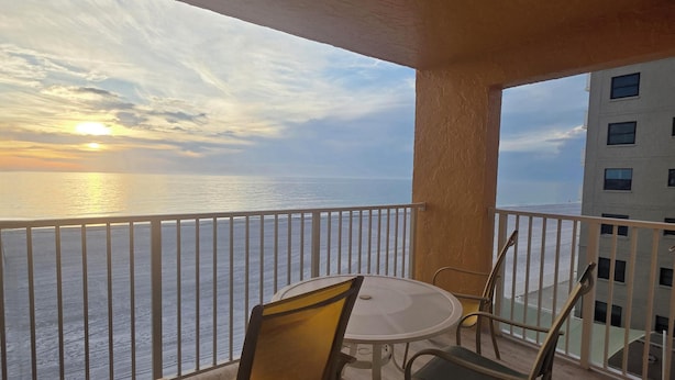 Ein Balkon mit Tisch und Stühlen, mit Blick auf ein Gewässer und ein Gebäude.