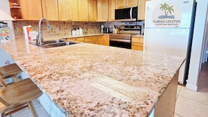 Eine moderne Küche mit Holzschränken, einer Granitabdeckung, Edelstahlgeräten und einem Schild für Florida Lifestyle Vacation Rentals.
