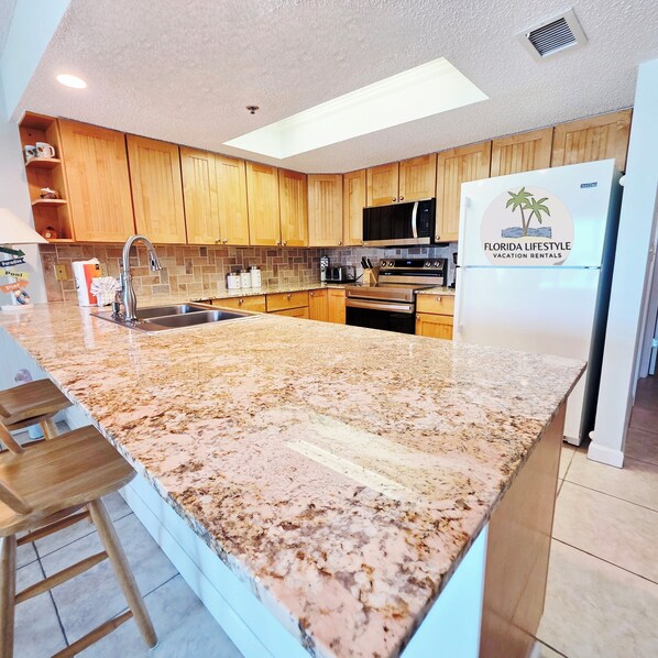 A modern kitchen with wooden cabinets, a granite countertop, stainless steel appliances, and a sign for Florida Lifestyle Vacation Rentals.
