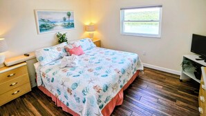 A bedroom with a bed, bedside tables, a desk, a TV, a window, and a painting on the wall.