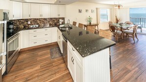 A modern kitchen with white cabinets, a black granite countertop, and a wooden floor.