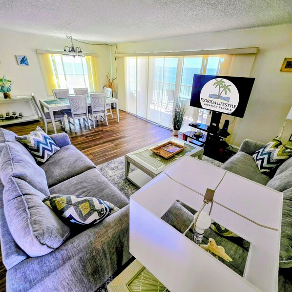A modern living room with grey sofas, a white coffee table, and a TV displaying 'Florida Lifestyle Vacation Rentals'.