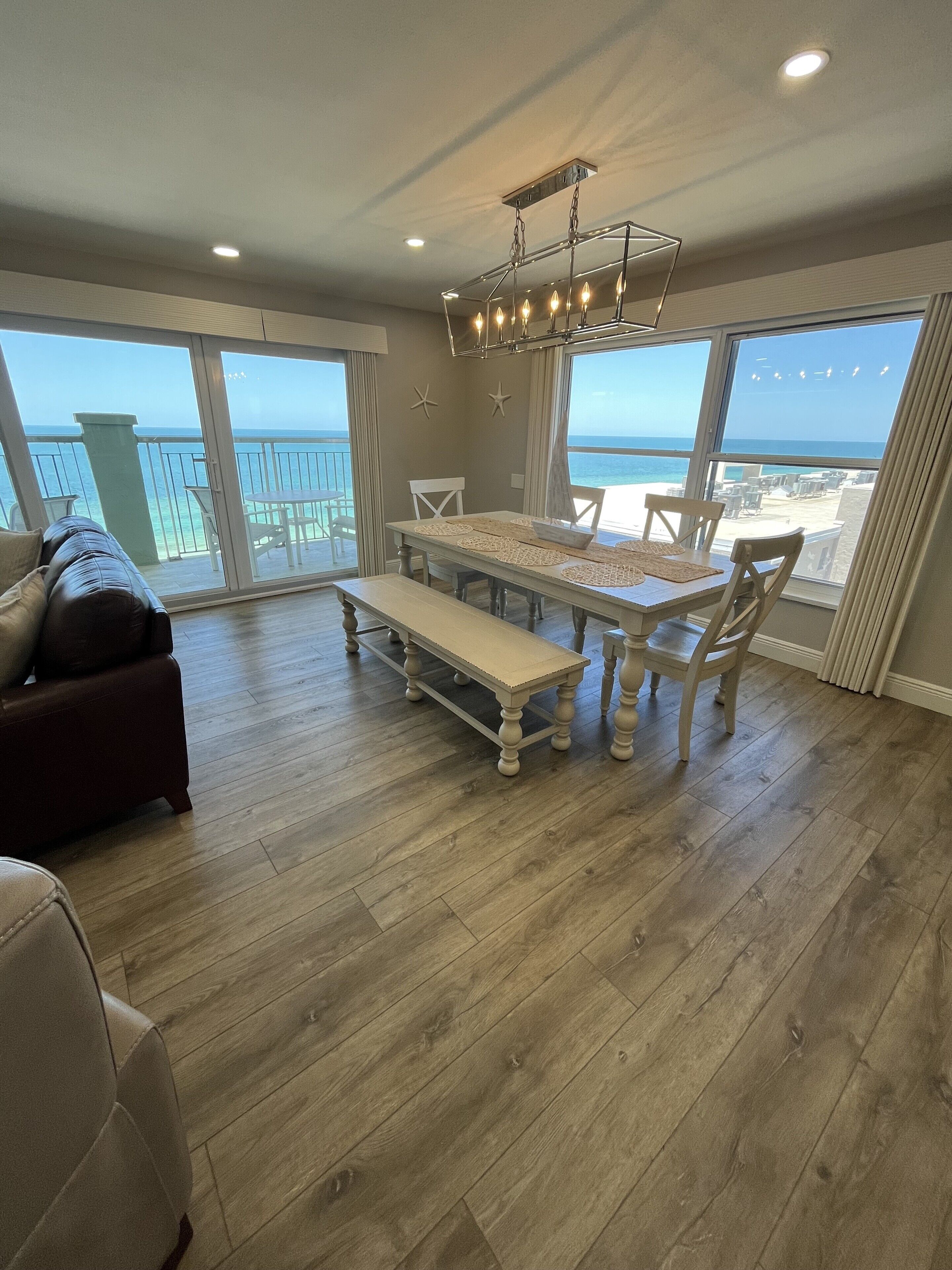 A spacious living area with a large dining table, a sofa, and a view of the beach.