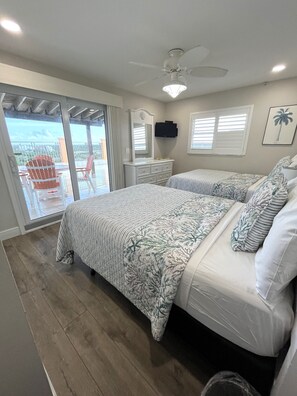 A bedroom with a bed, a dresser, a ceiling fan, and a view of the outdoors.