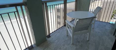 A balcony with a view of the beach and ocean, a table, and two chairs.
