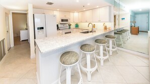 A modern kitchen with a central island, bar stools, and a microwave.