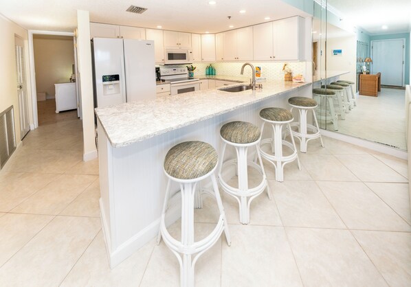 A modern kitchen with a central island, bar stools, and a microwave. - Holiday Villas III- 710 Intercoastal view! Low rates all 2026! (Indian Shores)