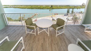 A balcony with a view of a body of water, a table, and two chairs.