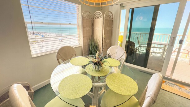 Comedor con mesa de vidrio, sillas de mimbre y vista a la playa a través de amplios ventanales.