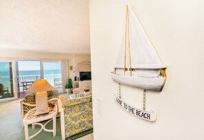 A living room with a view of the sea, a sailboat decoration, and a sign that reads "GONE TO THE BEACH".