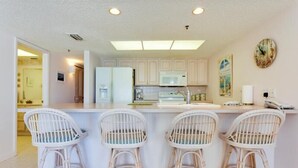 Una cocina moderna con armarios blancos, una isla central con taburetes altos, un microondas y un refrigerador.
