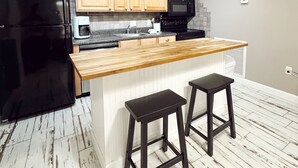A modern kitchen with wooden cabinets, a black refrigerator, a microwave, and a wooden island with two stools.