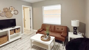 A living room with a white ceiling fan, a brown sofa, a white coffee table, a black chair, and a television on a white stand.