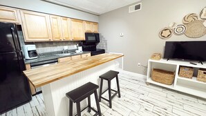 A modern kitchen with wooden cabinets, a black refrigerator, a microwave, and a wooden island with two stools.