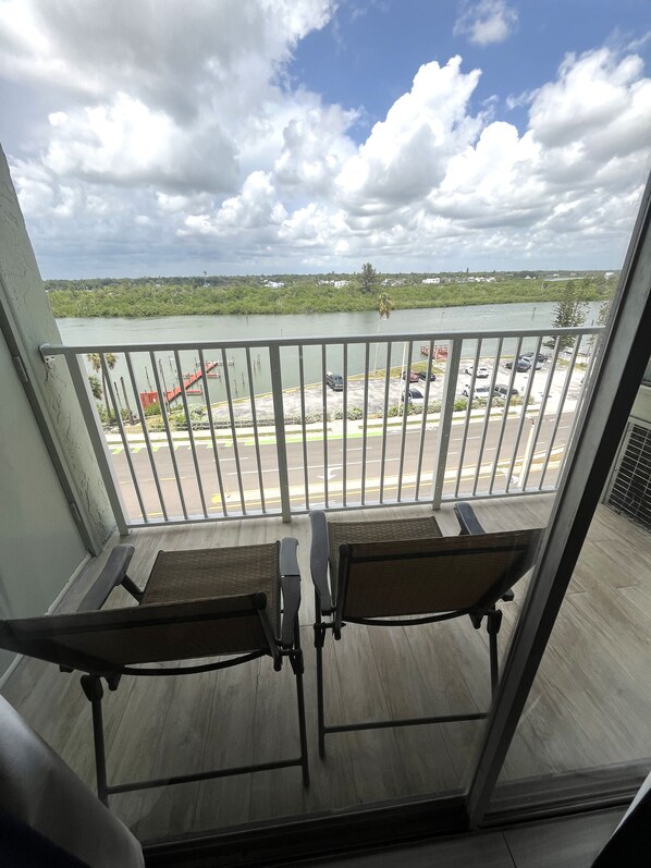 A balcony with two chairs, a view of a body of water, a parking lot, and a cloudy sky.