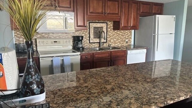 Una cocina con encimeras de granito, armarios de madera, un refrigerador blanco y una cafetera.