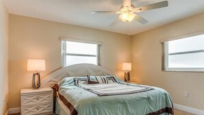 A bedroom with a bed, two bedside lamps, a ceiling fan, and two windows.