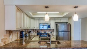 A modern kitchen with white cabinets, a stainless steel refrigerator, a built-in oven, and a microwave.