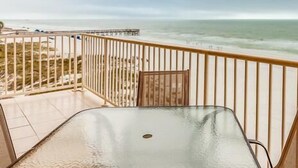 A balcony with a glass table and chairs, overlooking a beach and ocean.