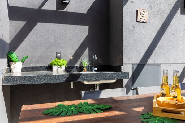 A modern outdoor kitchen with a built-in sink, potted plants, and a wooden table with a leaf decoration. - Casa com 2 suítes AC Higienópolis (São Paulo)