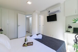Een hotelkamer met een bed, een televisie, een airconditioner en een bureau met een computer.
