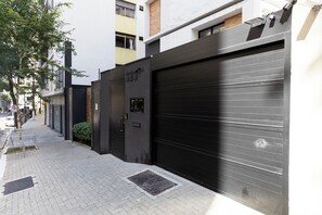 A modern building with a closed garage door, a visible door number, and a paved sidewalk. - Casa com 2 suítes AC Higienópolis (São Paulo)