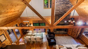 A spacious loft with a high ceiling, wooden beams, a dining area with a table and chairs, a fireplace, and a cozy seating area with a sofa and armchairs. - Log Cabin, Lake, Hot Tub, Near Wineries & Hiking (Dahlonega)