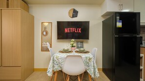 A modern kitchen with a black refrigerator, a wall-mounted TV displaying "NETFLIX," and a dining table set for two. - Skyline Stay in Araneta Cubao w/ Karaoke & Netflix  (Quezon City)