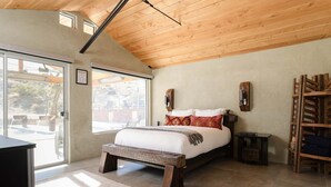 Un dormitorio con una cama grande, techo de madera y vistas al exterior.