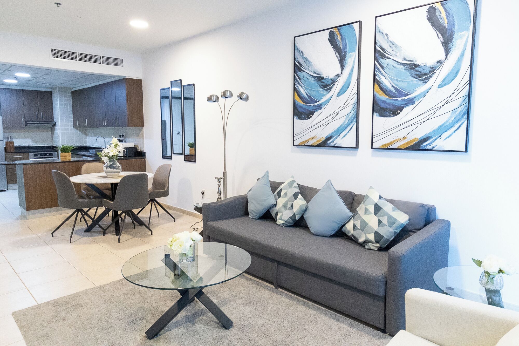 Ein modernes Wohnzimmer mit einem grauen Sofa, einem Glastisch und abstrakter Kunst an der Wand.