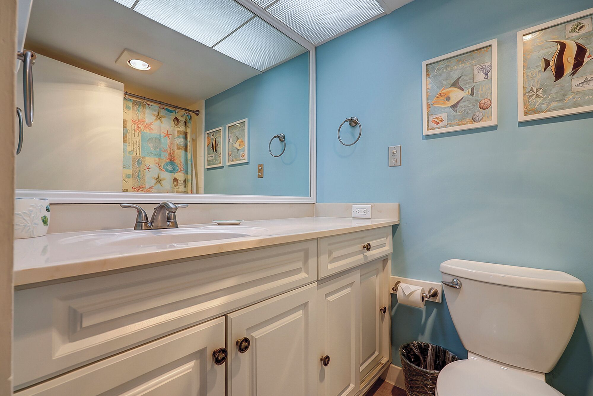 A bathroom with a large mirror, a sink, a toilet, and decorative wall art.