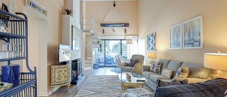A spacious living room with a sofa, coffee table, and a TV. There is a staircase leading to an upper level.