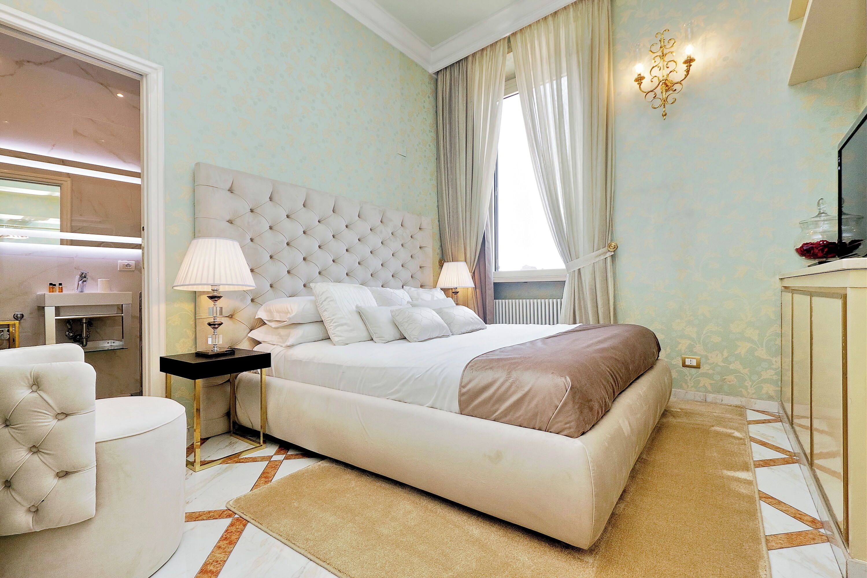 Une chambre avec un grand lit, une table de chevet avec des lampes, une chaise ronde blanche et une vue sur la salle de bain.
