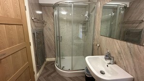 Ein modernes Badezimmer mit Duschkabine aus Glas, einem weißen Waschbecken und einer Holztür.