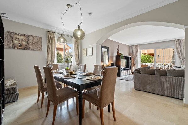A dining area with a table set for six, surrounded by chairs. There is a sofa and a TV in the background. - RDR446 - Gorgeous 3 bedroom Santa Maria Golf (Marbella)