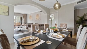 A dining area with a long table set for a meal, featuring a modern chandelier, a potted orchid, and a wine bottle. - RDR446 - Gorgeous 3 bedroom Santa Maria Golf (Marbella)