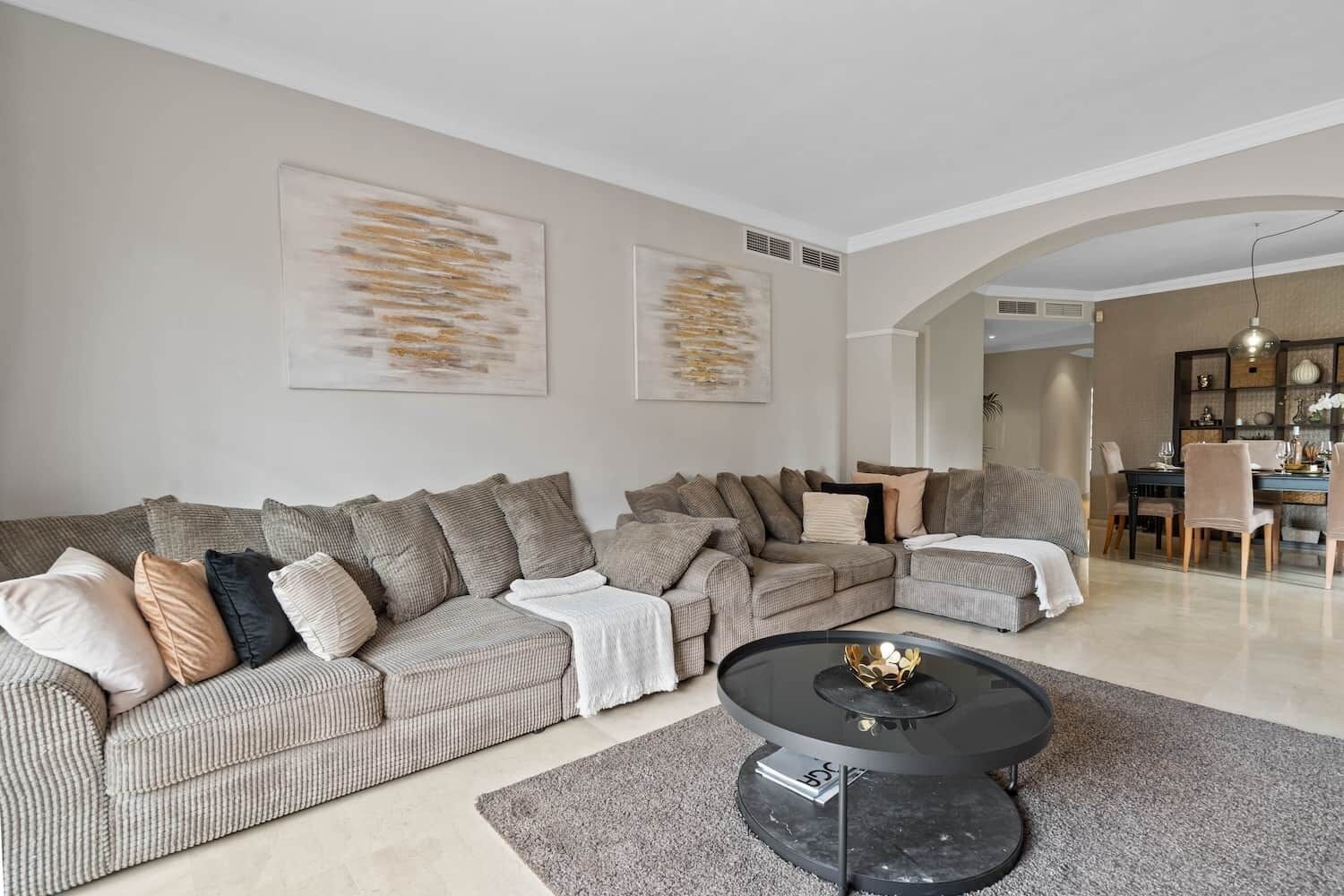 Una sala de estar moderna con un sofá modular, una mesa de centro redonda y un comedor con mesa y sillas.