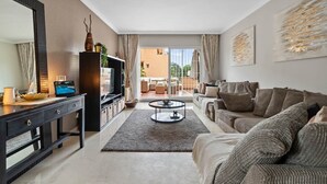 A modern living room with a sofa, a coffee table, and a TV on a black cabinet. There is a large mirror on the left and a painting on the right wall. - RDR446 - Gorgeous 3 bedroom Santa Maria Golf (Marbella)
