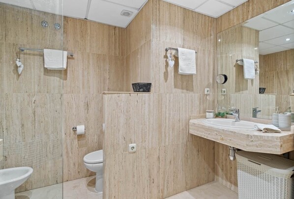 A modern bathroom with a large mirror, a sink with toiletries, and a toilet.