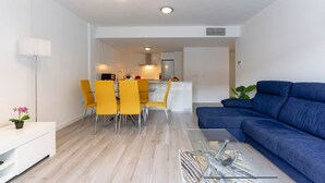 A modern living room with a blue sofa, a glass coffee table, and a dining area with yellow chairs. - RDR450 - Beautiful family apartment in Benahavis (Benahavís)