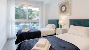 A hotel room with two beds, a large window with a view of trees and buildings, a decorative wall piece, and a small table with a lamp. - RDR450 - Beautiful family apartment in Benahavis (Benahavís)