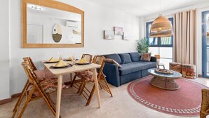 A modern living room with a dining area, a sofa, a round coffee table, and a large mirror.